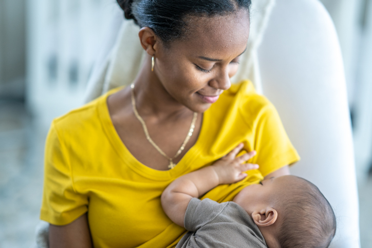 Baby hängt an der Brust der Mutter. Foto: FatCamera/iStock – FatCamera/iStock