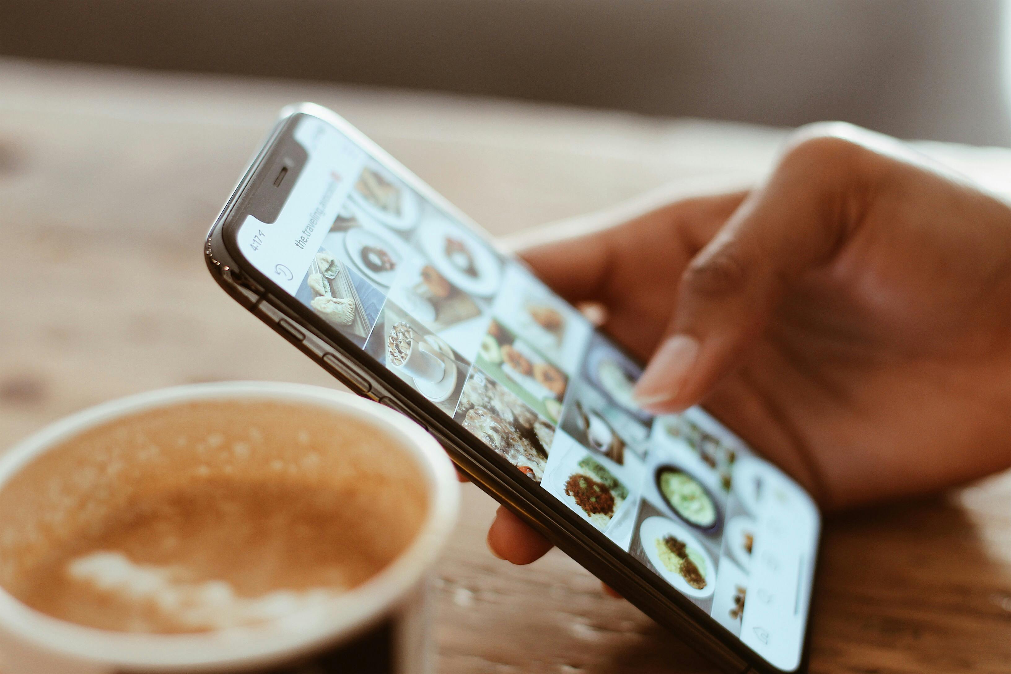 Hand mit Smartphone, daneben ein Kafeebecher. Foto: Kerde Severin/Pexels – Kerde Severin/Pexels